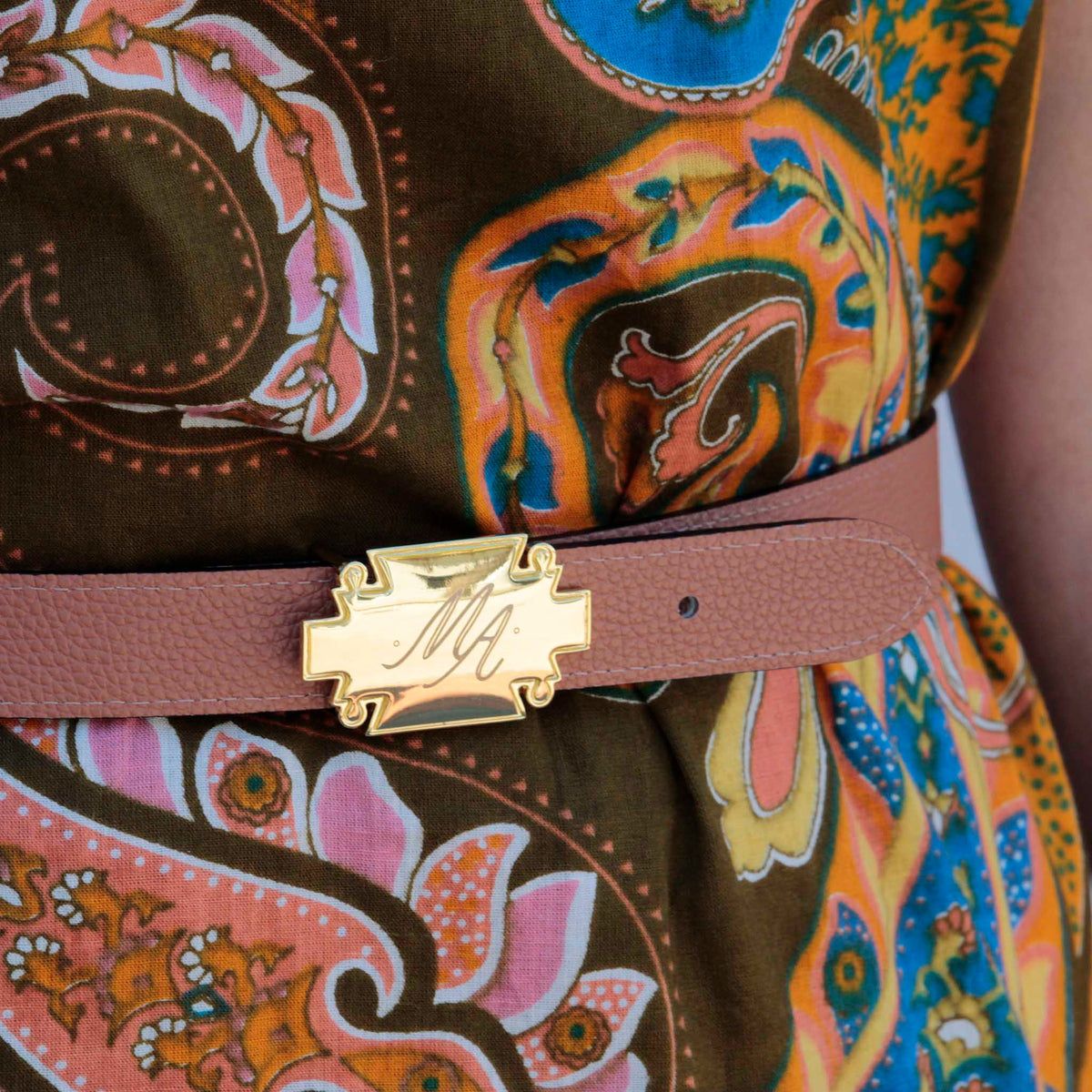 Saddle brown pebbled leather belt strap worn with a paisley print dress, fastened with a gold plaque buckle engraved with a monogram.