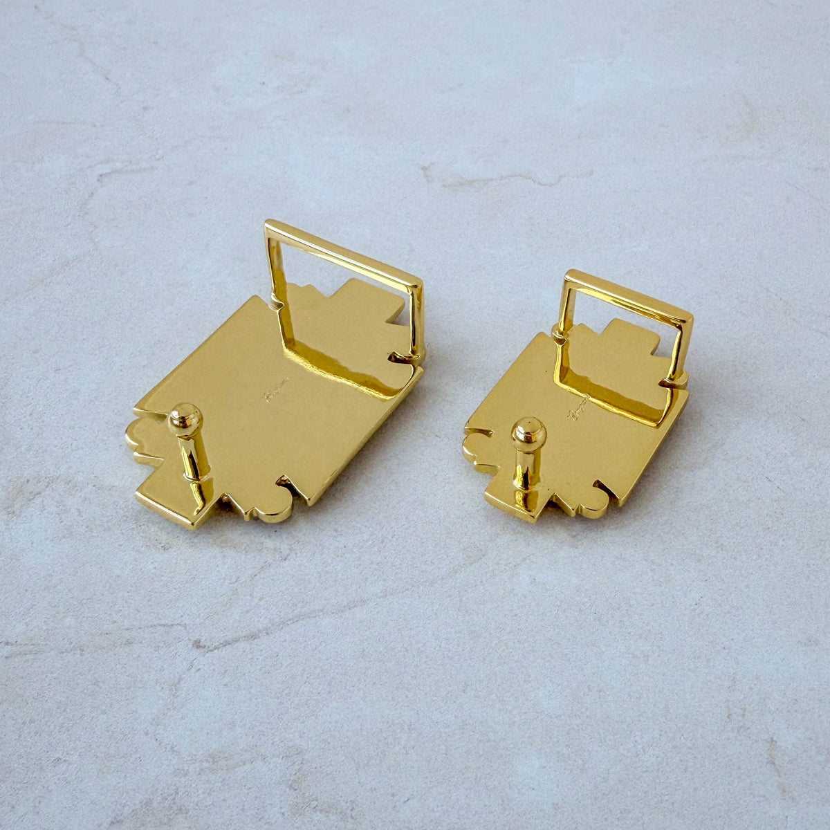 Back view of two sizes of gold-plated belt buckles, showing the fixed loops and fastening pins.