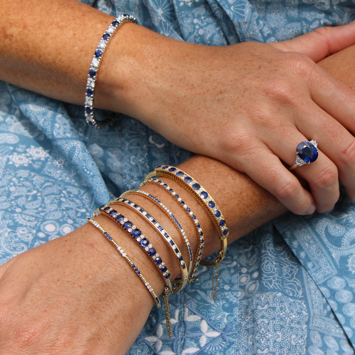 A close up of a person wearing a sapphire ring and stacked sapphire bangles and bracelets.
